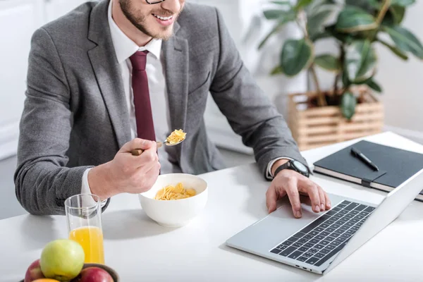 Businessman working on laptop while eating breakfast at kitchen — Stock Photo