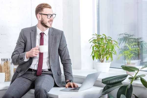 Geschäftsmann in Gläsern sitzt auf Arbeitsplatte und trinkt Kaffee in der Küche — Stockfoto