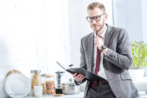 Pensive businessman holding notebook and pen at kitchen — Stock Photo