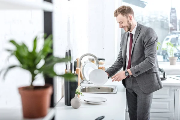 Smiling businessman washing dishes in kitchen at home — Stock Photo