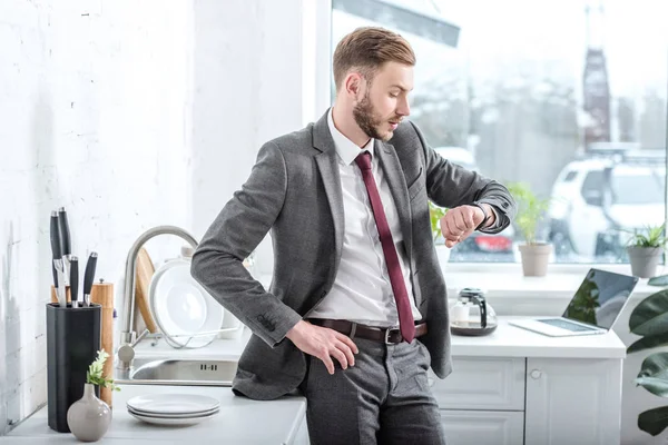 Successful handsome businessman looking at watch in kitchen — Stock Photo