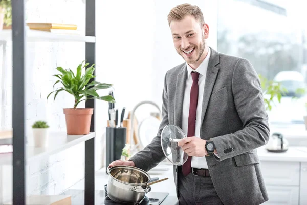 Homem de negócios sorrindo no desgaste formal segurando panela e se preparando para cozinhar na cozinha — Fotografia de Stock