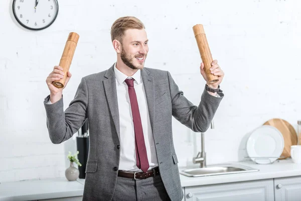 Smiling excited businessman holding pepper pots and getting ready to cook in kitchen — Stock Photo