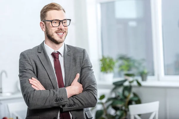 Handsome businessman in glasses with arms crossed looking away — Stock Photo