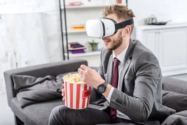 Hombre de negocios en el sofá en realidad virtual auriculares viendo la película y comer palomitas de maíz - foto de stock