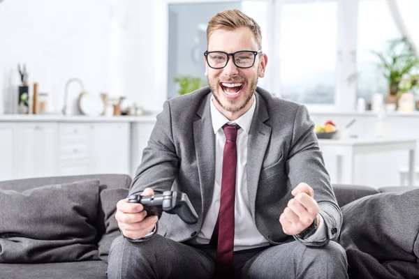 Excited businessman holding console and playing video game at home — Stock Photo