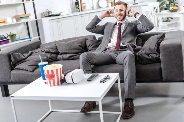 Улыбающийся бизнесмен в наушниках сидит и отдыхает на диване дома — стоковое фото