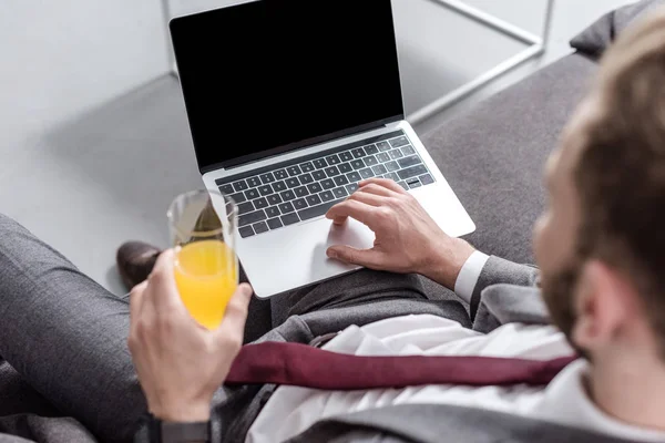 Vista recortada de hombre de negocios beber jugo de naranja y el uso de ordenador portátil con pantalla en blanco - foto de stock