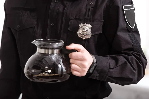 Vista recortada del oficial de policía sosteniendo maceta de vidrio de café filtrado en caliente - foto de stock