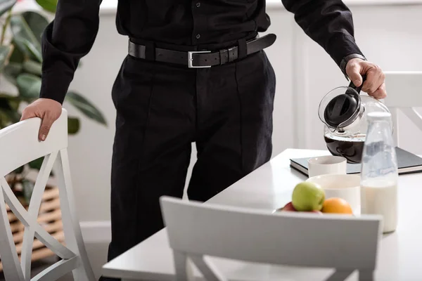Vista parcial del policía vertiendo café filtrado de maceta de vidrio en la cocina - foto de stock