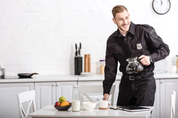 Sonriente guapo policía sosteniendo vaso de café filtrado a la hora del desayuno - foto de stock