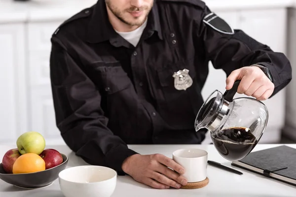 Обрезанный вид на офицера полиции, наливающего фильтрованный кофе из стеклянного горшка на кухне утром — стоковое фото