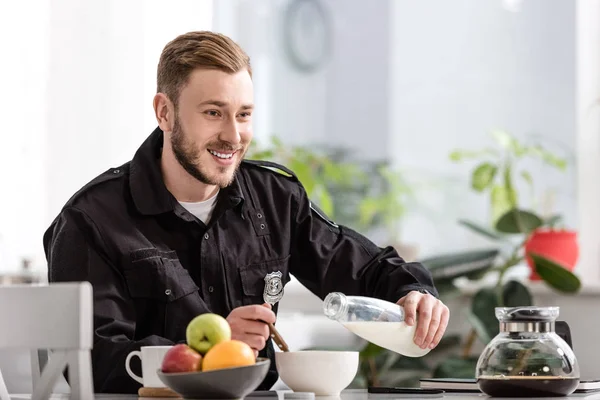 Poliziotto sorridente versando il latte nella ciotola dei cereali e facendo colazione in cucina — Foto stock