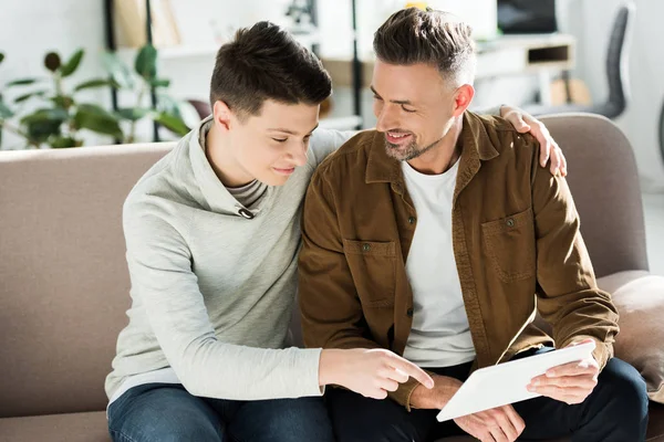 Lächelnder Vater und Teenager-Sohn schauen zu Hause auf Tablet — Stockfoto