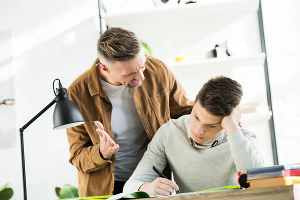 Angry father yelling at teen son, boy covering ears — Stock Photo