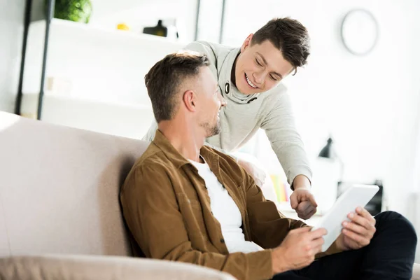 Smiling father and teen son using tablet and looking at each other at home — Stock Photo