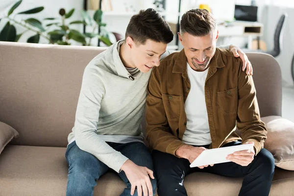 Fröhlicher Vater und Teenager-Sohn schauen zu Hause auf Tablet — Stockfoto