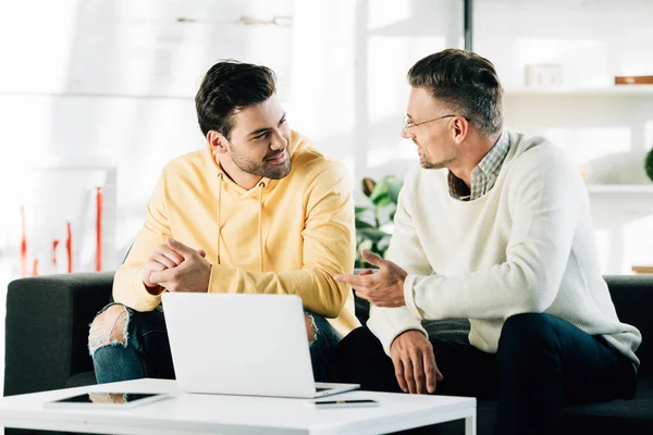Son and mature father sitting neat table with laptop and talking at home — Stock Photo