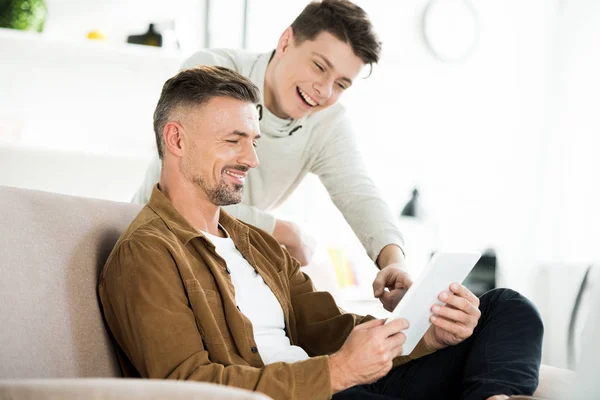 Glücklicher Teenager-Sohn zeigt zu Hause auf Vater-Tablet — Stockfoto