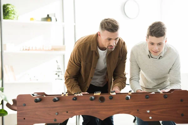 Father and teen son playing table football at home during sunny day — Stock Photo