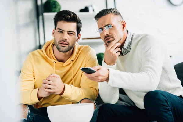 Pensive son and mature father watching tv together on weekend at home — Stock Photo