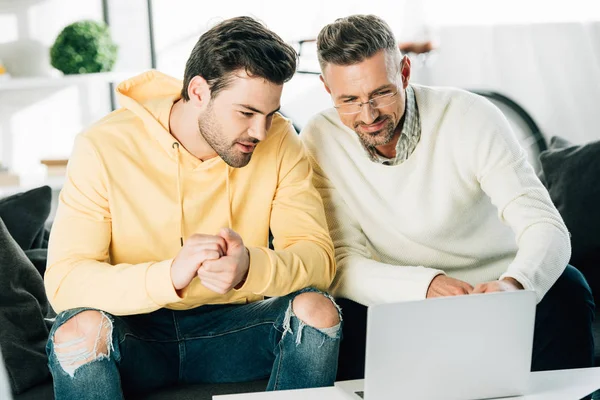 Son and mature father looking at laptop on sofa at home — Stock Photo