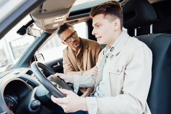 Handsome father supporting teen son while teaching him driving car — Stock Photo