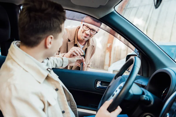 Happy handsome father giving car key to teen son on street — Stock Photo