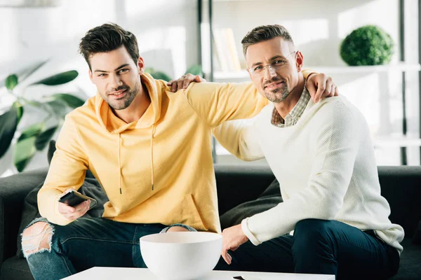 Son and mature father hugging and watching tv together on weekend at home — Stock Photo