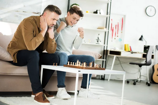 Lächelnder Teenie-Sohn gewinnt Schach, während er mit Vater zu Hause spielt — Stockfoto