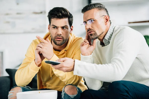 Sérieux fils et mature père regarder la télévision ensemble le week-end à la maison — Photo de stock