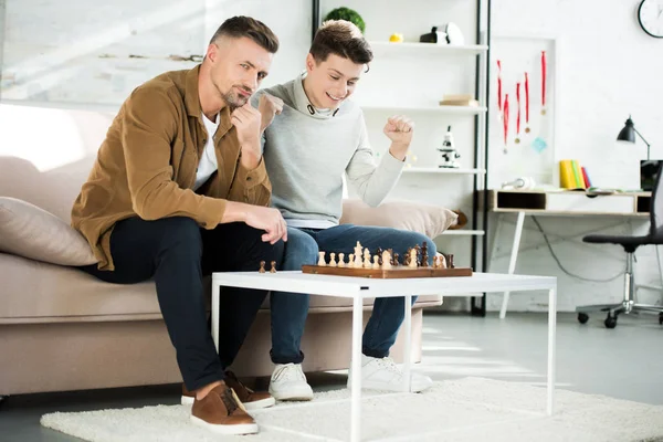 Feliz hijo adolescente ganar ajedrez mientras juega con el padre en casa - foto de stock