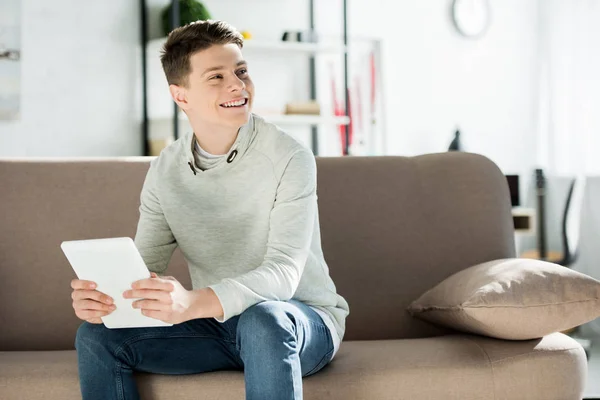 Adolescente sonriente sosteniendo la tableta en el sofá en casa y mirando hacia otro lado - foto de stock