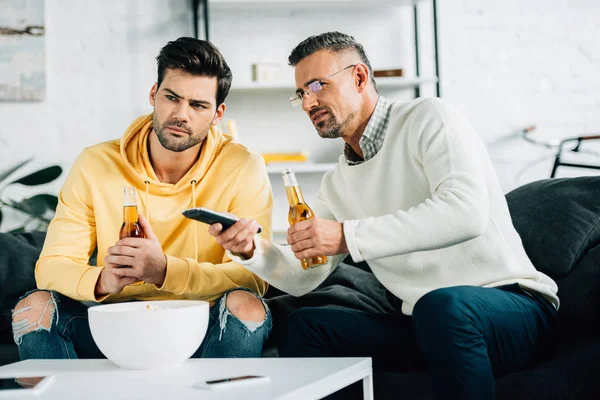 Hijo y padre maduro viendo tv con cerveza en fin de semana en casa - foto de stock