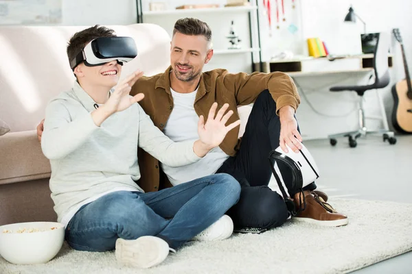 Father looking at teen son watching something with virtual reality headset at home — Stock Photo