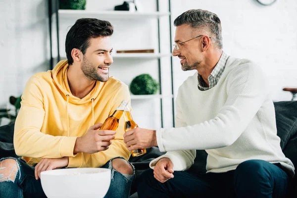 Happy son and mature father clinking with bottles of beer on weekend at home — Stock Photo