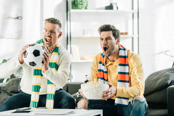 Excited son and father with scarfs watching football and screaming at home — Stock Photo