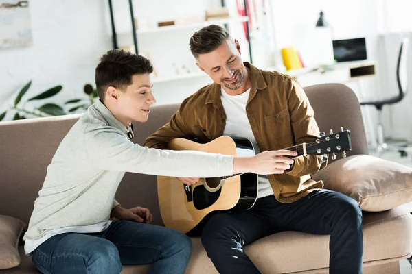 Teen son teaching father play acoustic guitar at home — Stock Photo