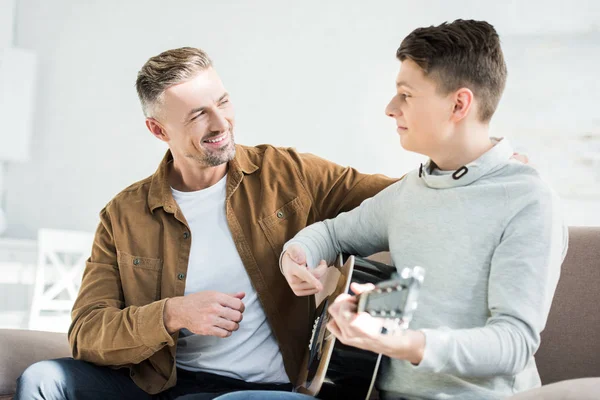 Teen son playing acoustic guitar for cheerful father at home — Stock Photo