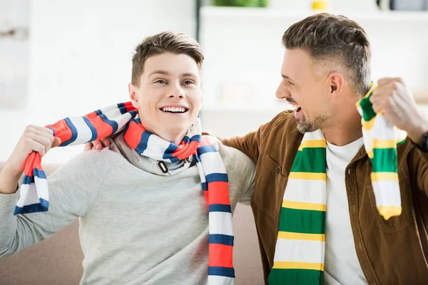 Aufgeregter glücklicher Vater und Teenager-Sohn in Schals schauen sich zu Hause ein Sportspiel an — Stockfoto