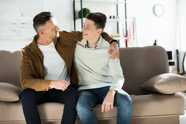 Glücklicher Vater und Teenager-Sohn, die sich zu Hause auf dem Sofa umarmen — Stockfoto