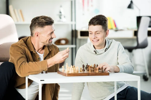 Lächelnder Vater zeigt Teenager-Sohn Schachfigur beim Schachspielen zu Hause — Stockfoto