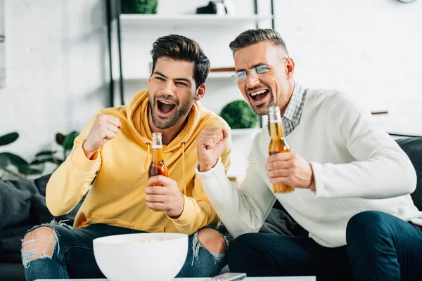 Excited son and mature father watching sport with beer on weekend at home — Stock Photo