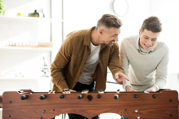 Feliz padre e hijo adolescente jugando futbolín en casa - foto de stock