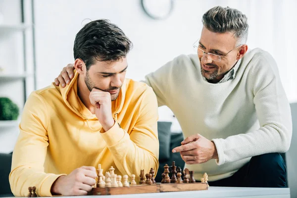 Hijo y padre maduro jugando ajedrez juntos en el fin de semana en casa - foto de stock
