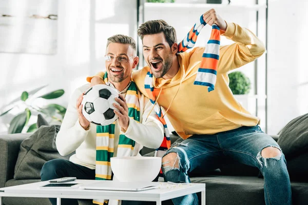 Excited son and mature father with scarfs watching football and screaming at home — Stock Photo