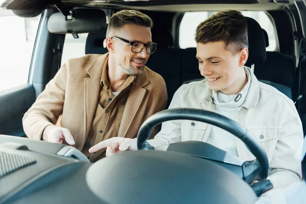 Smiling handsome father teaching teen son driving car — Stock Photo