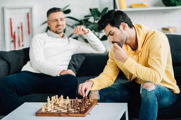 Маленький сын и взрослый отец играют в шахматы на выходных дома — стоковое фото
