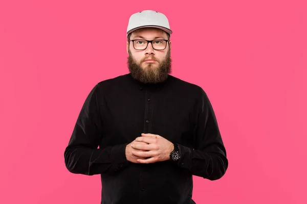 Серйозний бородатий чоловічий хіпстер у капелюсі та окулярах дивиться на камеру ізольовано на рожевому — стокове фото
