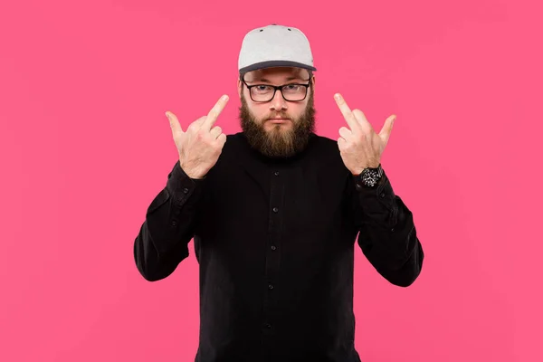 Стильный бородатый мужчина в очках, показывающий средний палец, изолированный на розовом — стоковое фото